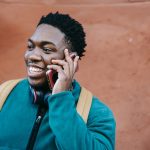 homem negro vestindo uma blusa manga longa azul sorrindo ao telefone