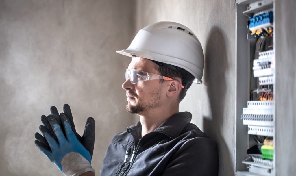 profissional de Engenharia Eletrotécnica de lado com capacete, óculos de proteção e luvas