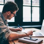 homem escrevendo com notebook na frente para ilustrar conteúdo sobre satisfação profissional