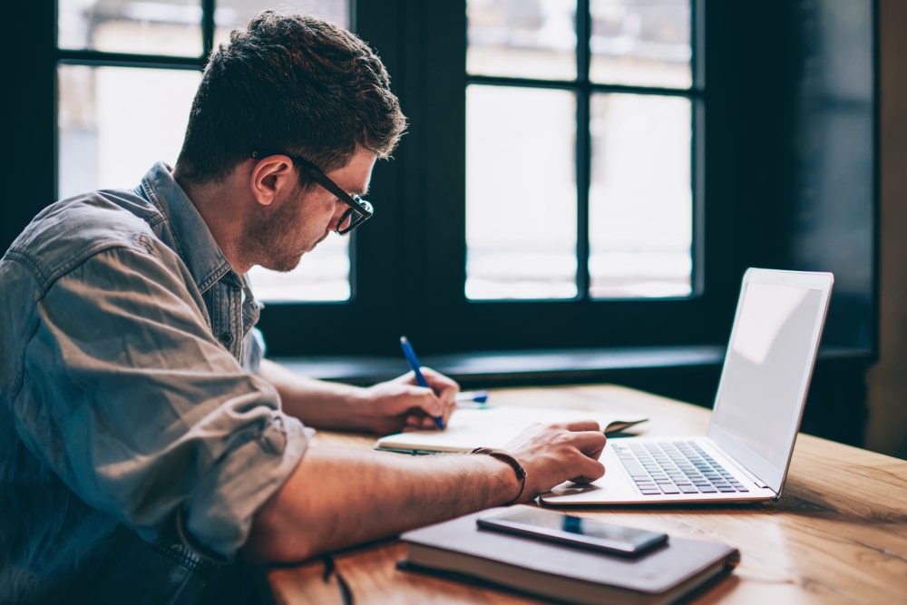 homem escrevendo com notebook na frente para ilustrar conteúdo sobre satisfação profissional