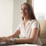 mulher sorrindo e digitando no notebook para indicar texto sobre o que fazer no primeiro dia de trabalho