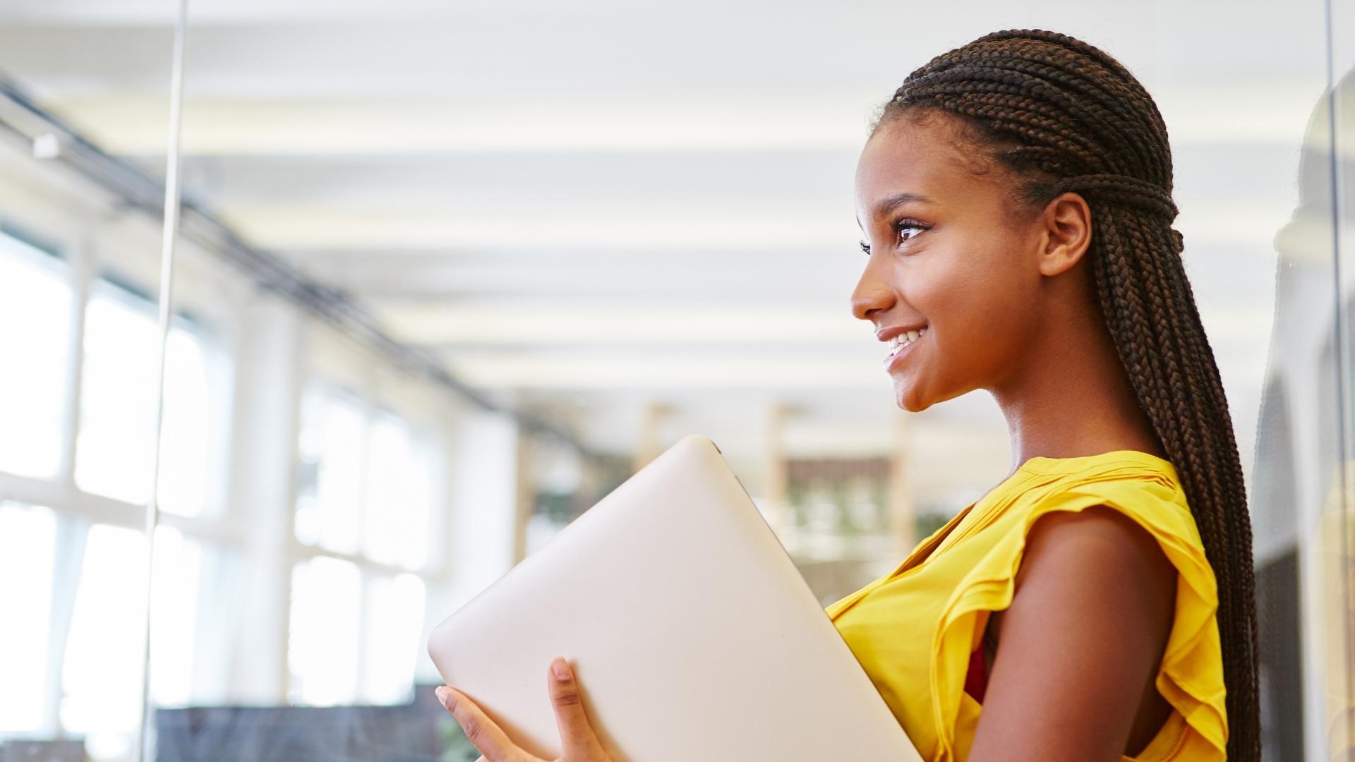 jovem de lado com notebook na mão para ilustrar texto sobre bolsa-auxílio