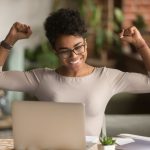 imagem de uma mulher negra feliz de frente para o notebook para ilustrar o texto de como conseguir um emprego