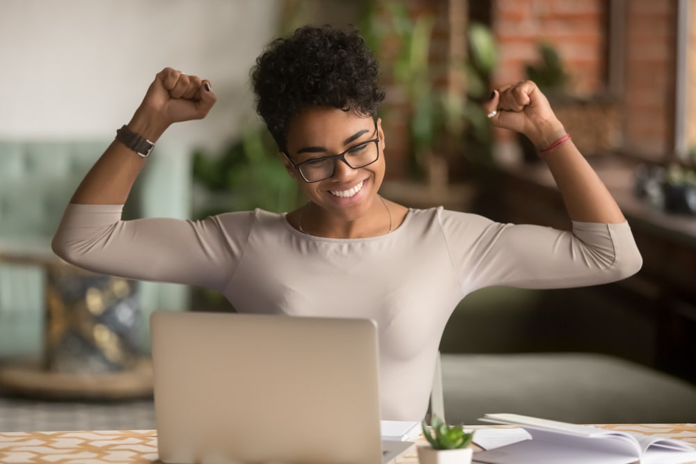 imagem de uma mulher negra feliz de frente para o notebook para ilustrar o texto de como conseguir um emprego