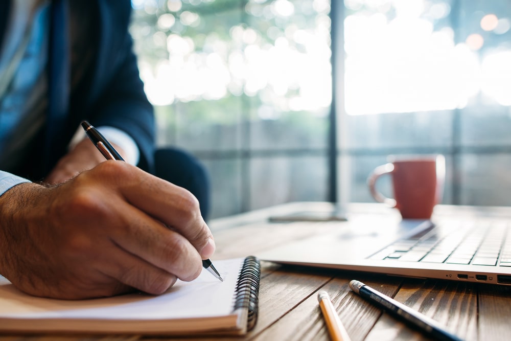 homem com bloco e notebook para ilustrar texto sobre anotar ideias em reuniões