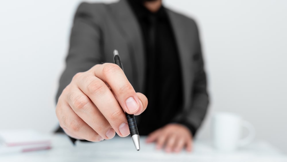 homem com mão na frente e caneta para ilustrar texto sobre Cuidados ao participar de processos seletivos